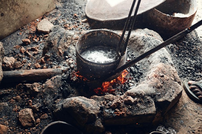 Close-up of an iron pot heating over open fire in a traditional metal forging process.