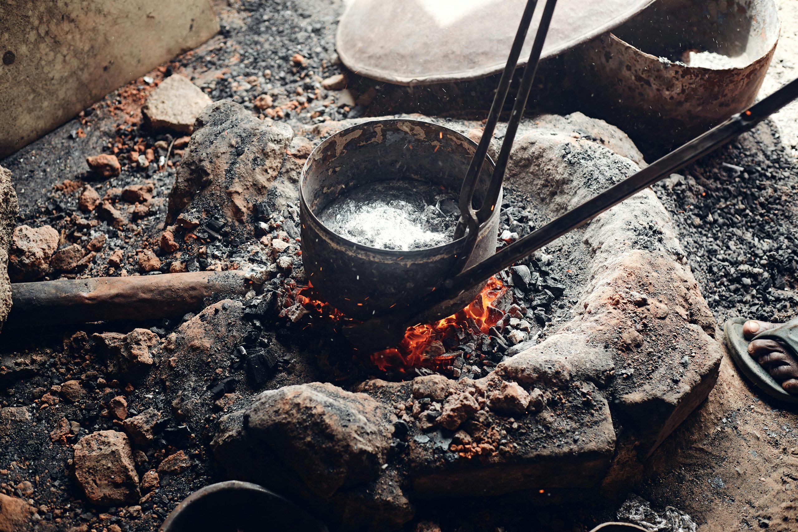 Close-up of an iron pot heating over open fire in a traditional metal forging process.