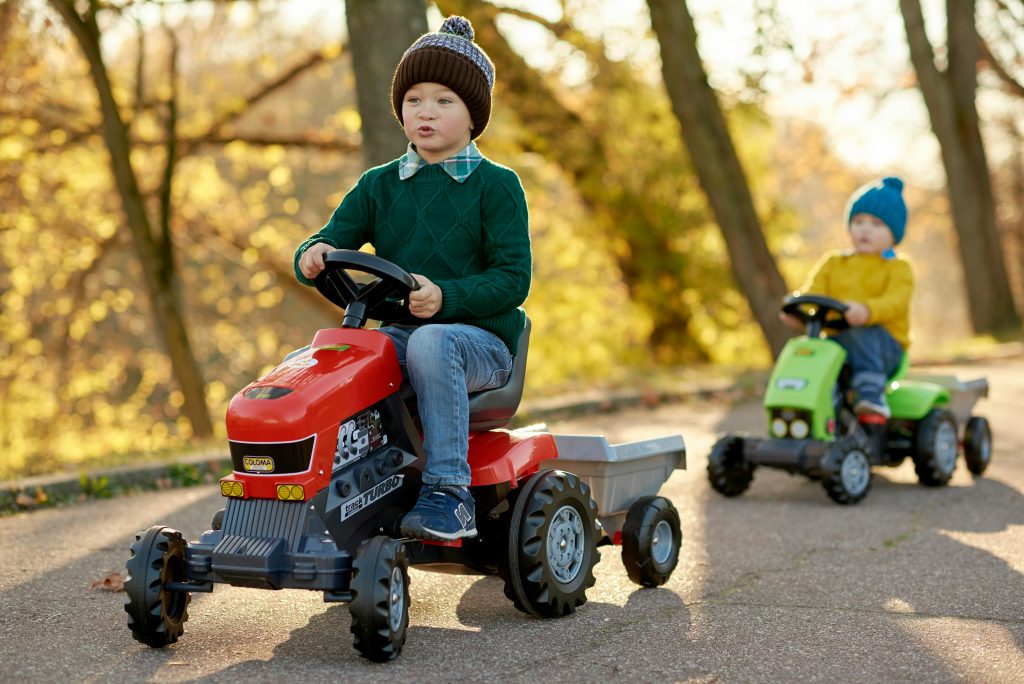 Two young boys enjoying a sunny day riding toy tractors in a park.