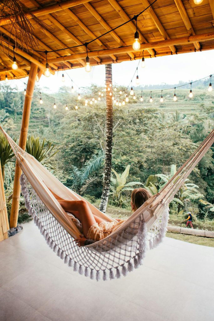 Woman lounging in a hammock on a serene tropical veranda surrounded by nature.