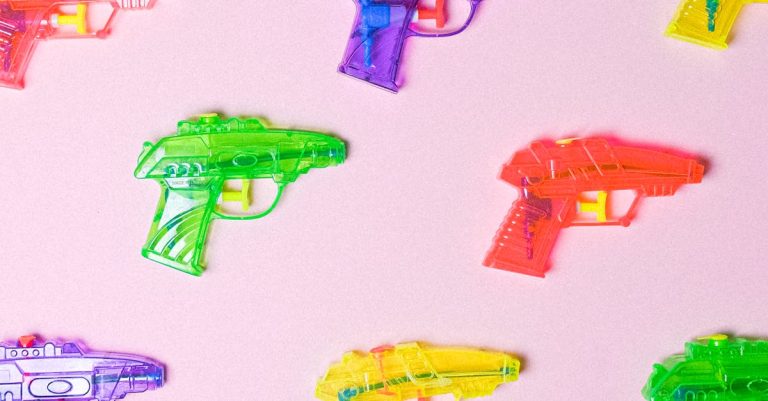 Colorful toy water guns on a pink background arranged in a pattern.