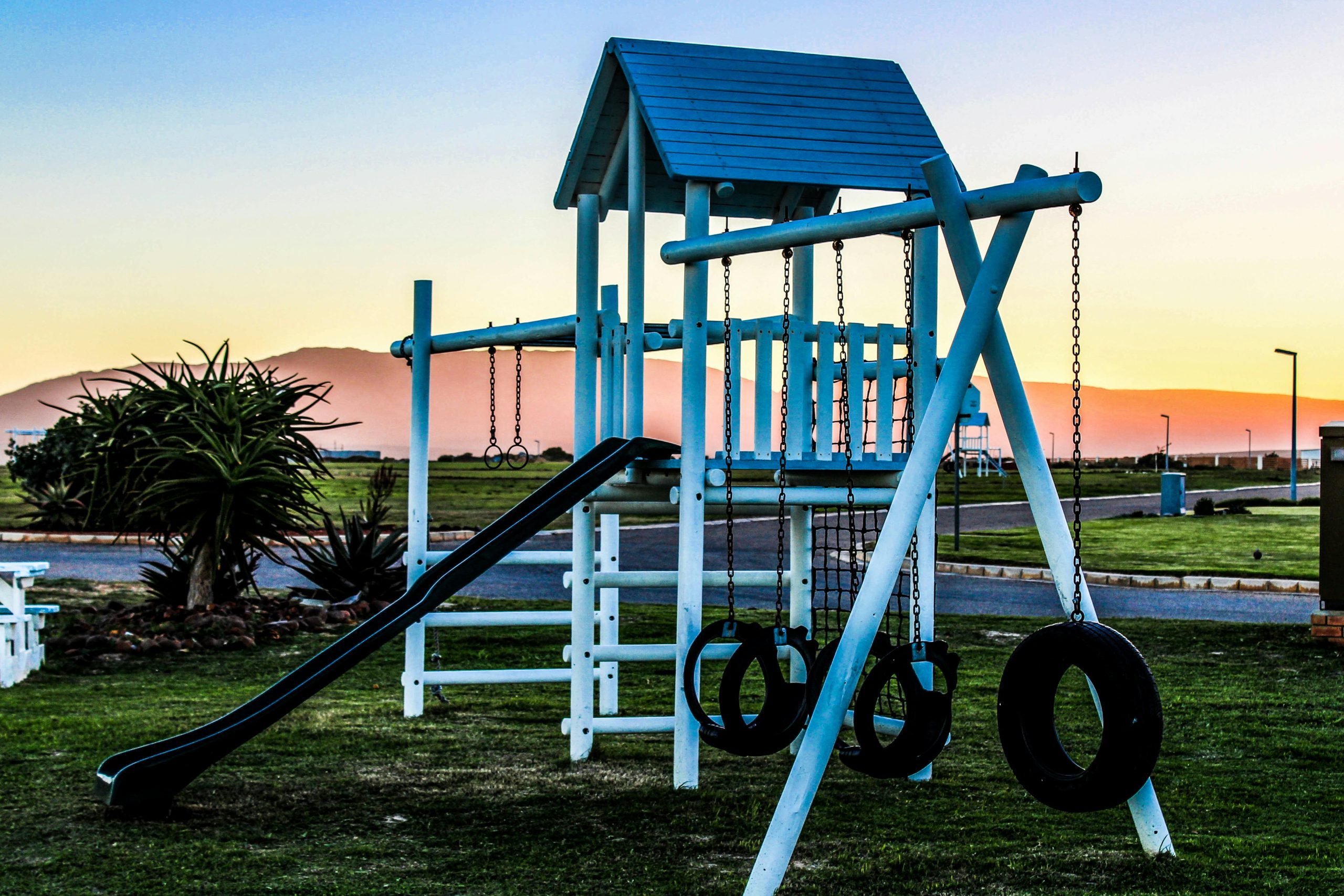 Outdoor playground with swings and slide captured at sunset, offering a serene view.