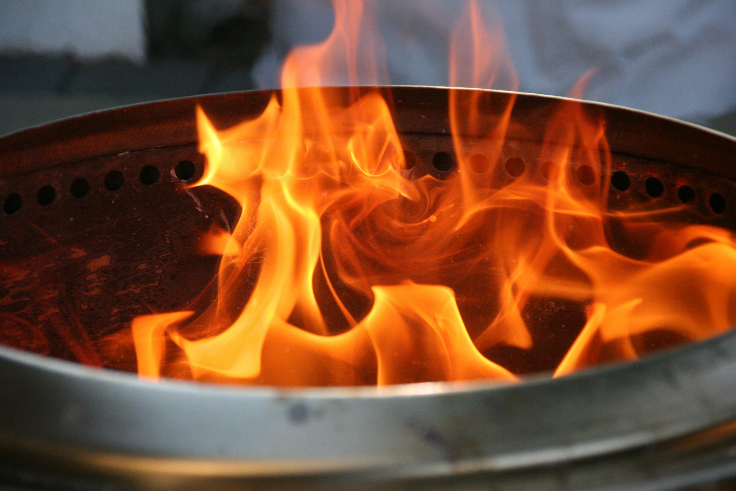 Close-up image of bright orange flames dancing inside a metal fire pit.