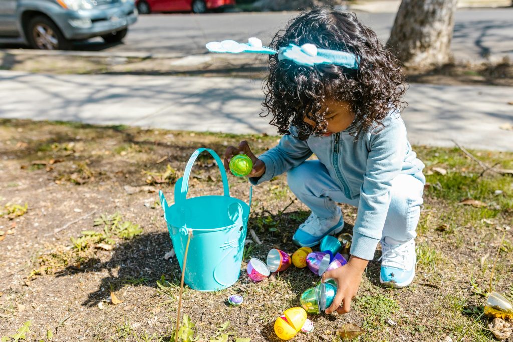Young child on an Easter egg hunt outdoors, gathering colorful eggs in a bucket.