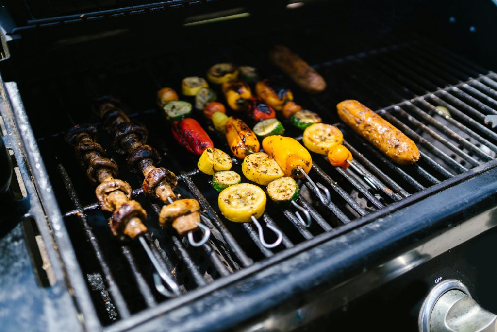 Colorful skewers with vegetables and sausages grilling on an outdoor barbecue.