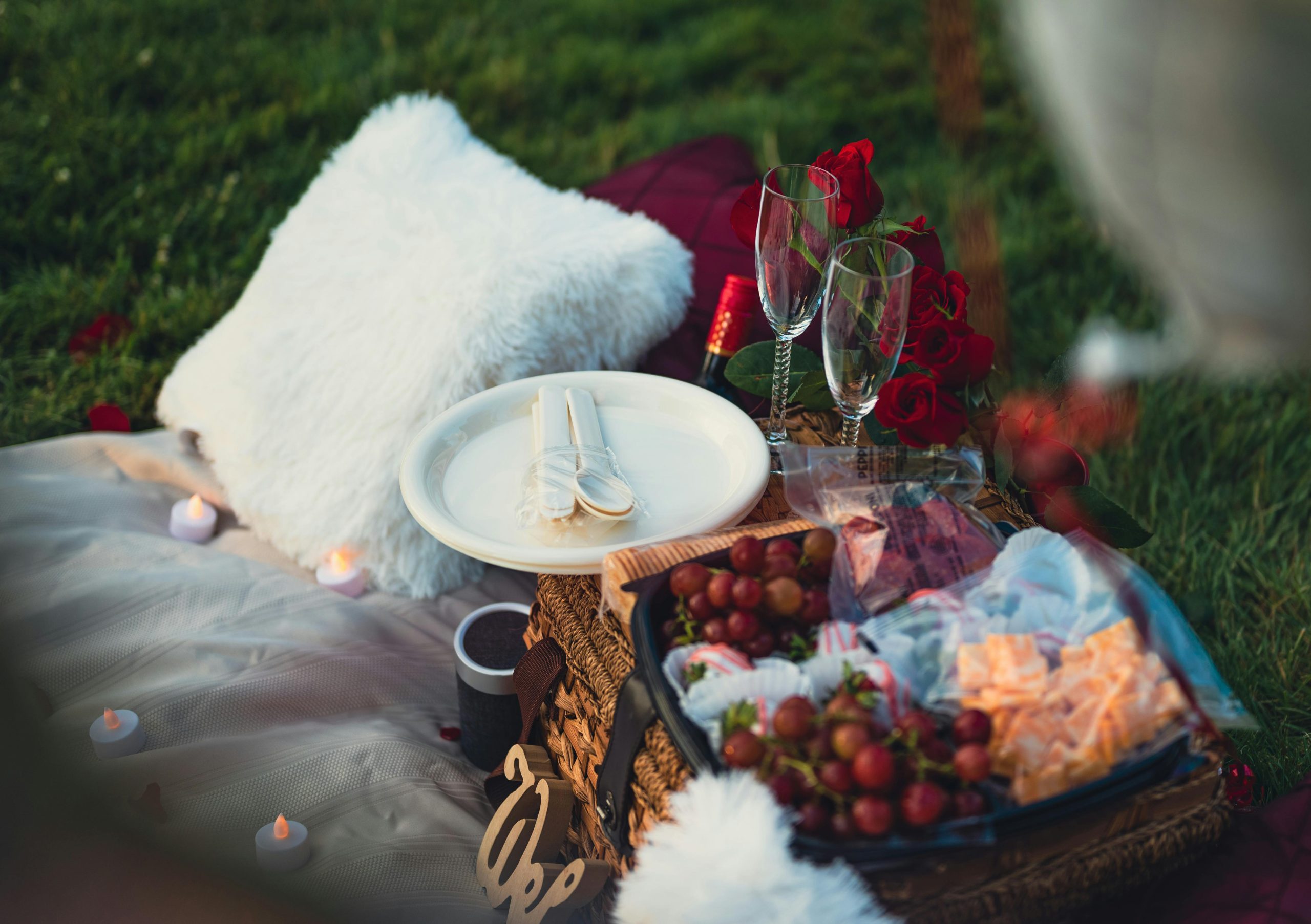Charming outdoor picnic scene featuring grapes, cutlery, cushions, and wine glasses on a blanket.